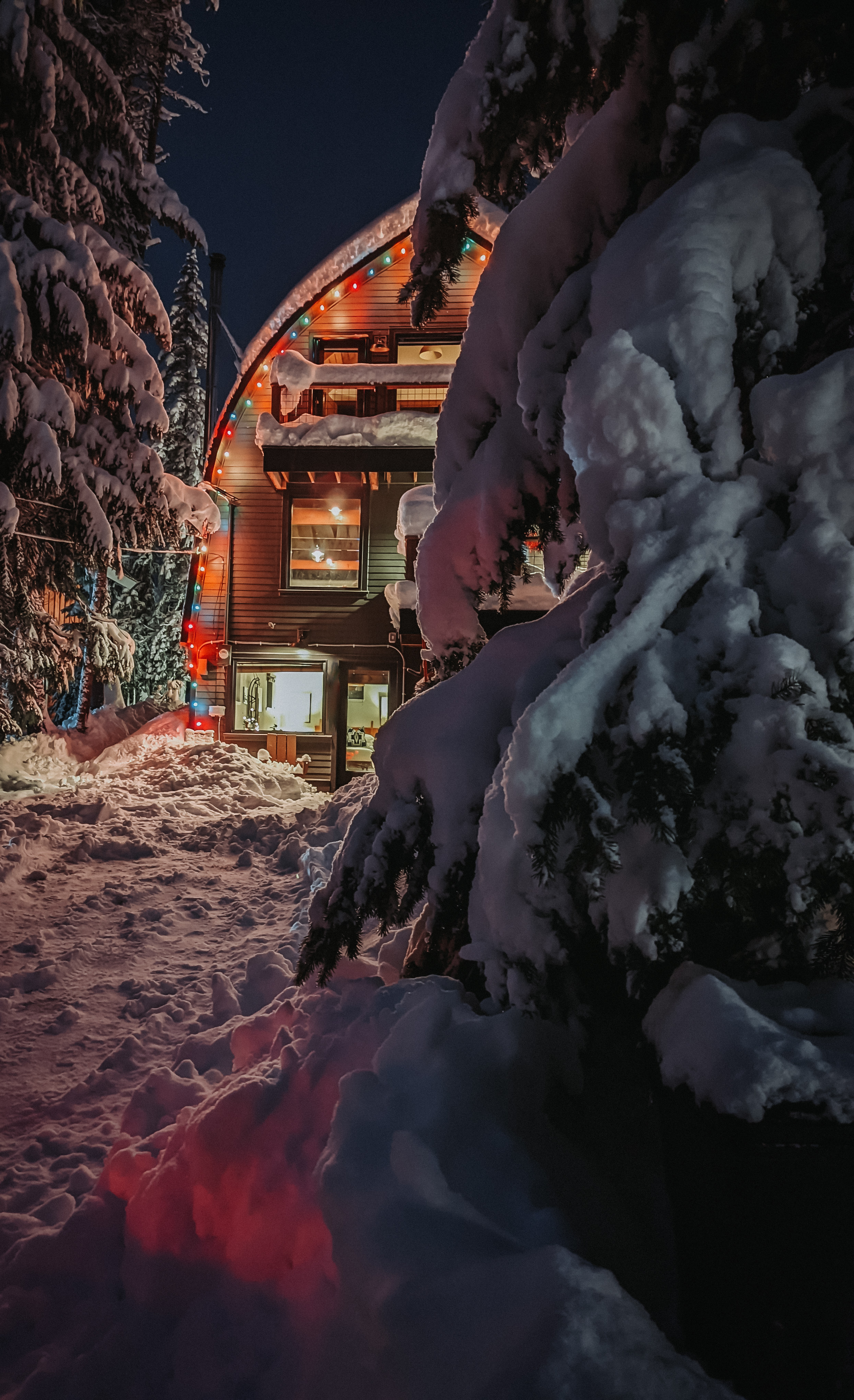 a snowy mountain cabin at night with holiday lights on it