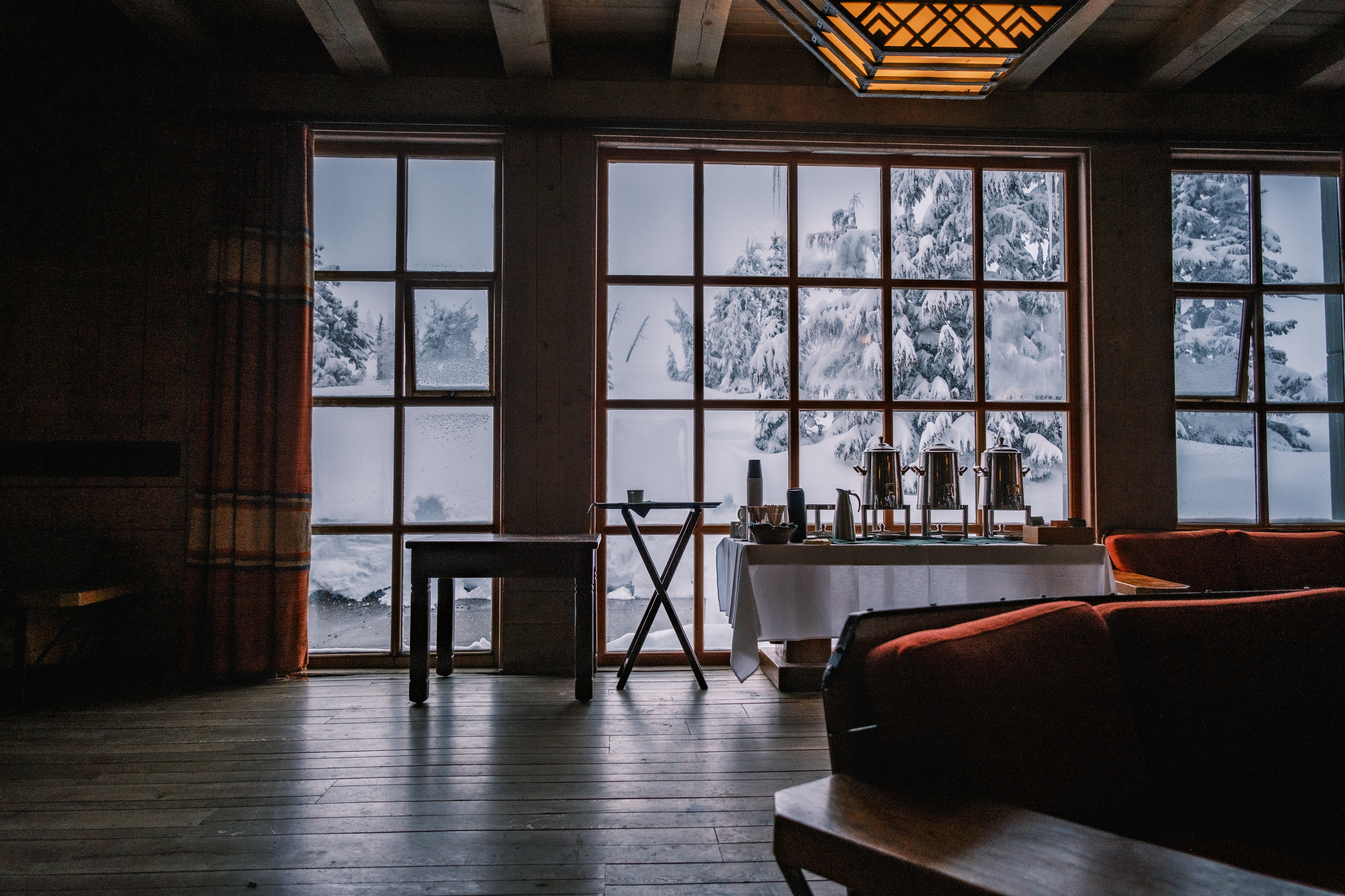 inside timberline lodge in the morning, there is a table of coffee and snow out the windows