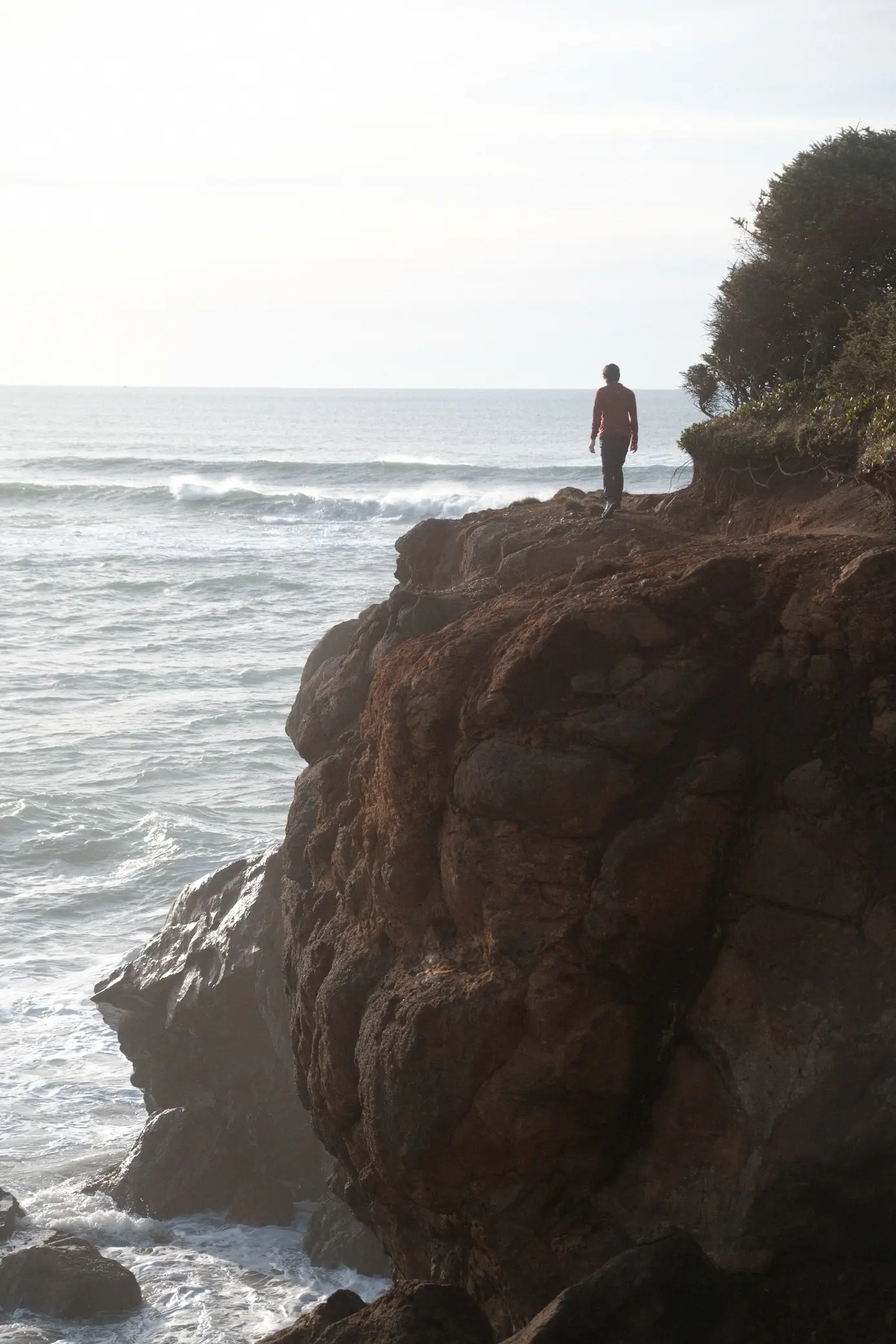 Person standing on rocky formation looking over the ocean with their back to the viewer
