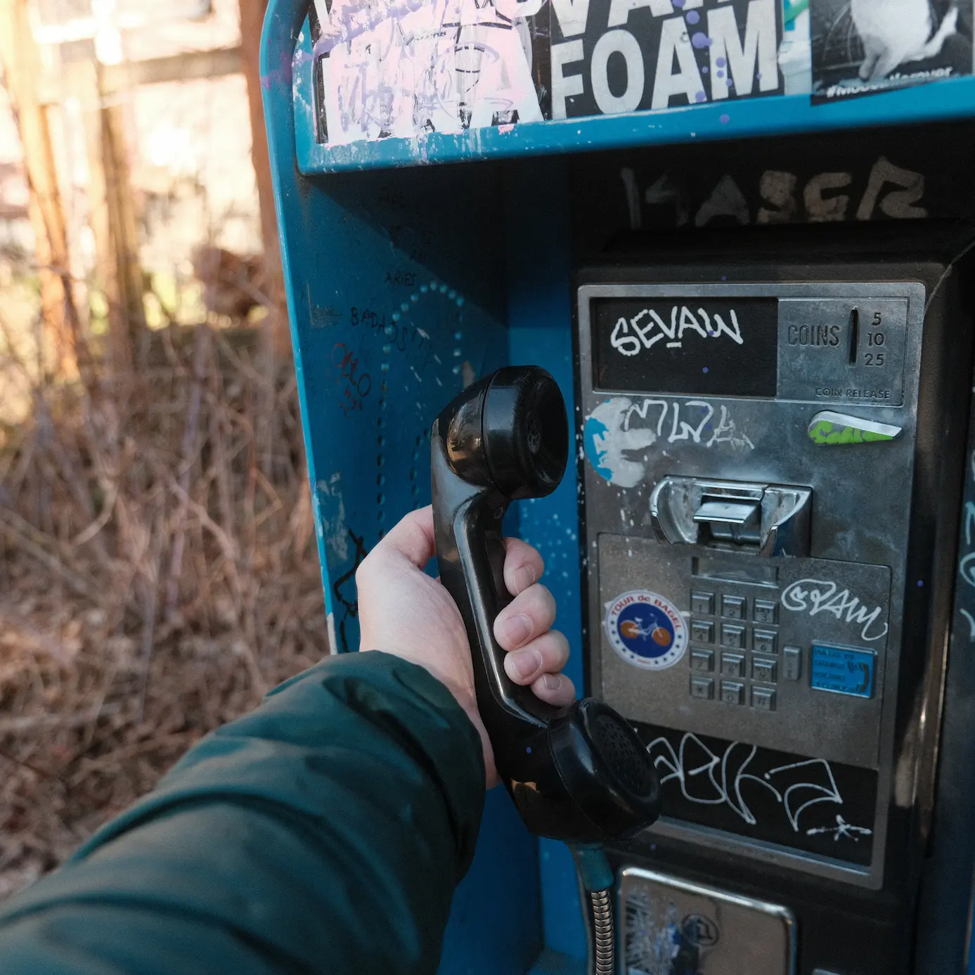 Photo of a payphone with a blue encasing and black handpiece in a person's hand