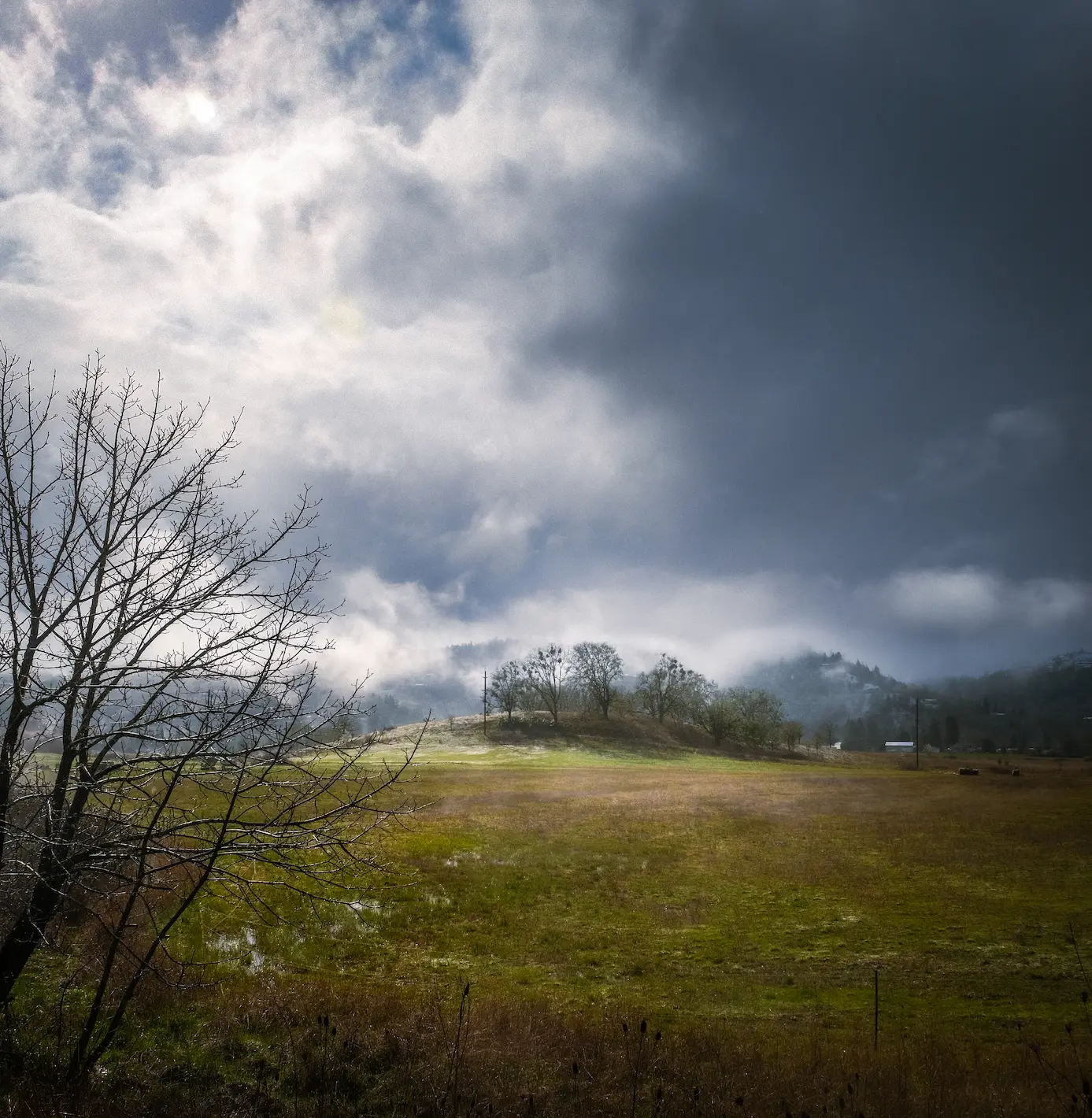 sun peeks through clouds as a misty day is captured with a rolling hill and patches of snow fills the frame