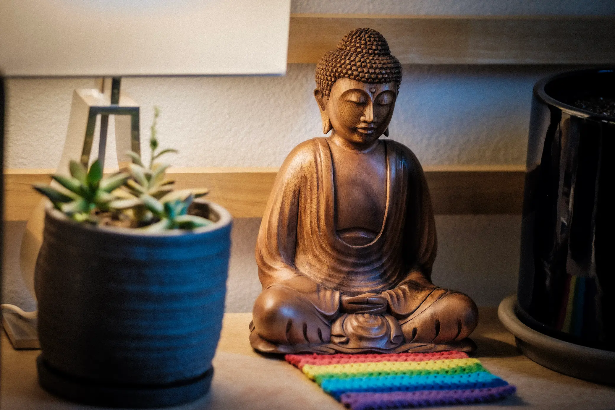 photo of a statue of the Buddha on shelf with a rainbow crocheted piece in front of it