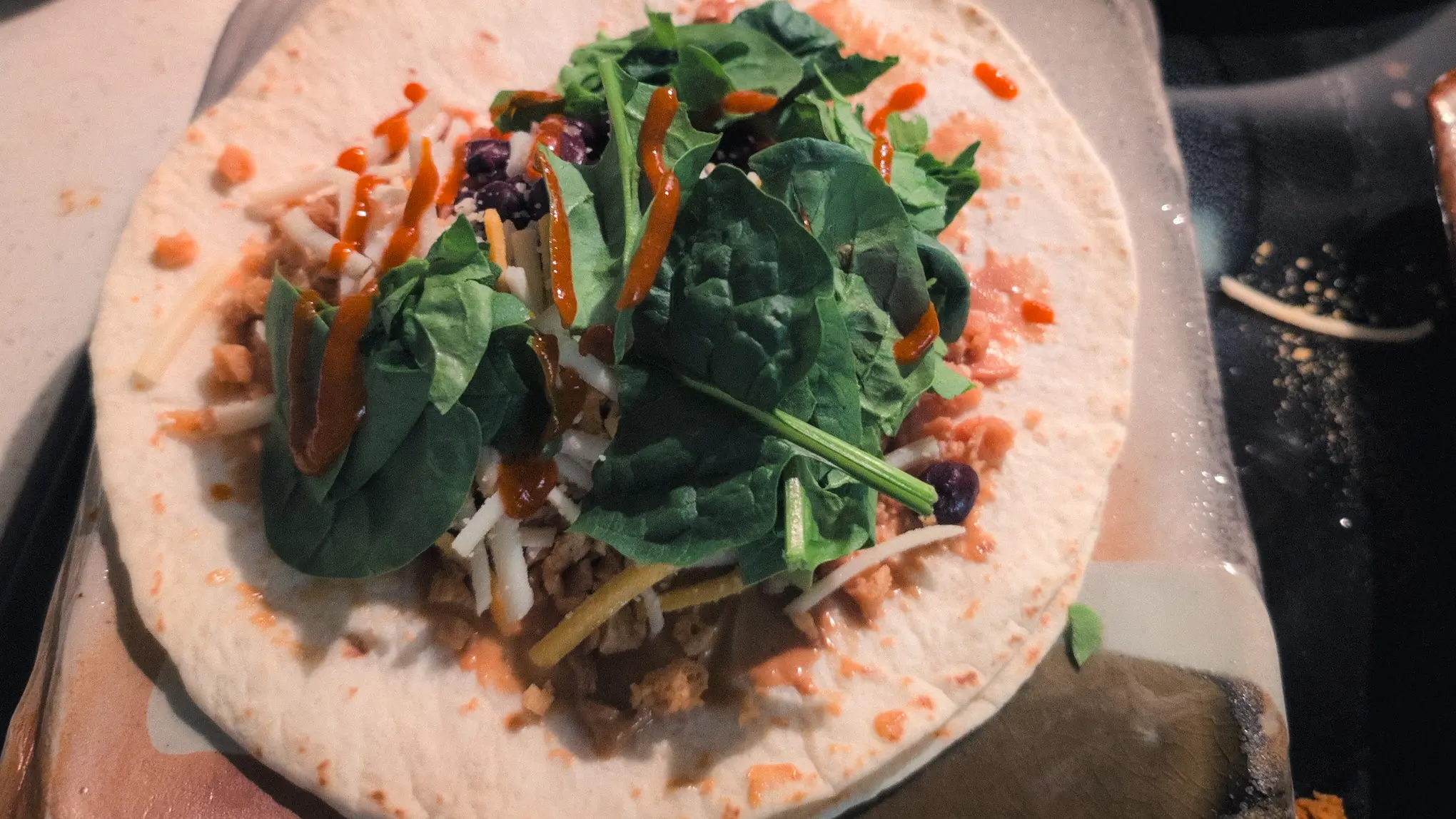 flour tortilla with peanut butter sriracha base, self-seasoned tvp, black beans, vegan cheese, spinach, and more sriracha