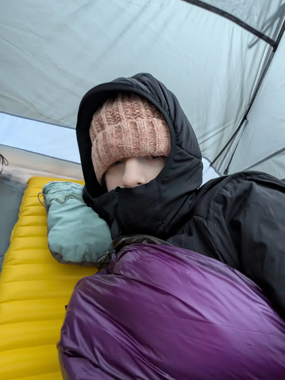 Person in sleeping bag and jacket with hood