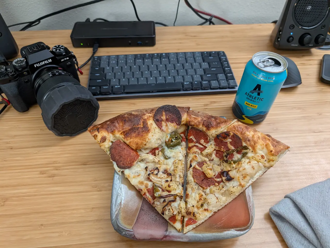 Image shows 2 pieces of pizza on a plate, Athletic Brewing NA beer can, and Fujifilm camera
